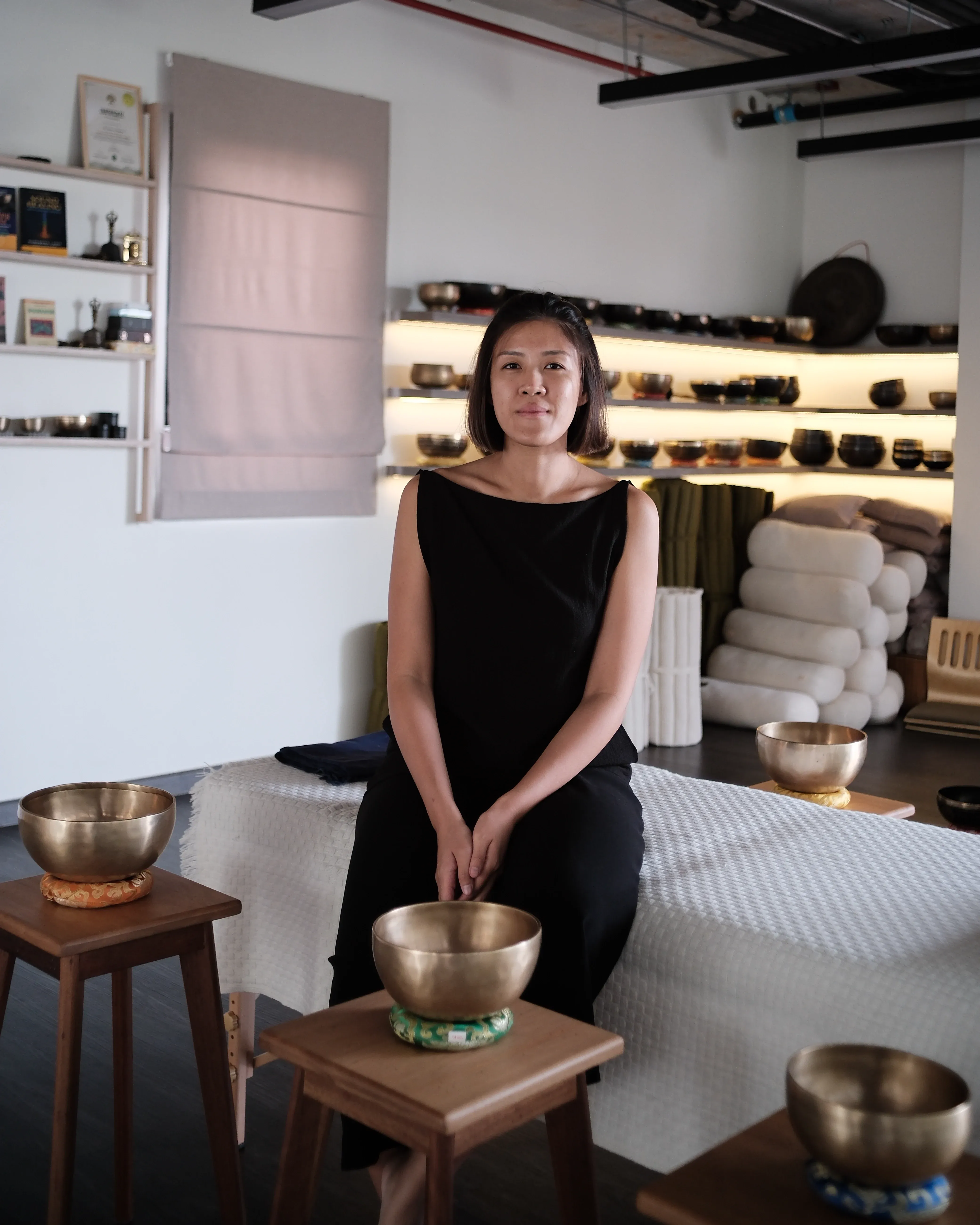 Ice standing in front of the lit singing-bowl shelves at Attuned Studio, Bangkok.